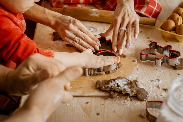 Vista lateral de perto das mãos do membro da família cortando diferentes formas de Natal de massa crua para assar biscoitos de gengibre festivos de Natal
