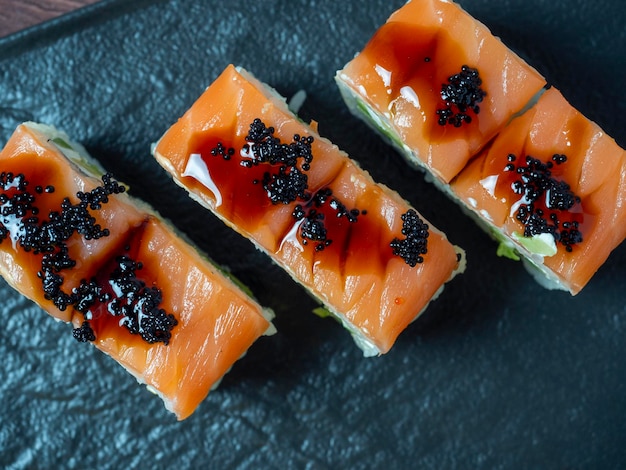 Vista lateral de suculentos rolos deliciosos decorados com caviar. Cozinha japonesa, prato preto, close-up, vista de cima, plano plano