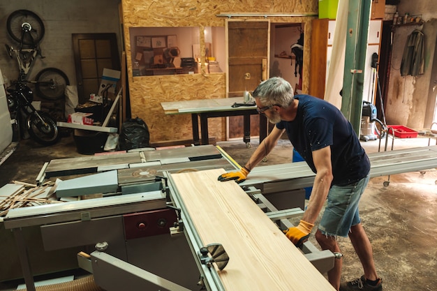 Foto vista lateral de um carpinteiro manipulando pedaços grandes de madeira em uma máquina de corte industrial