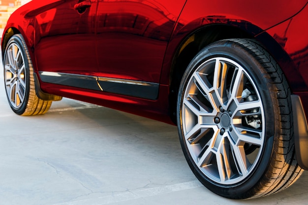 Foto vista lateral de um carro. pneu e roda de liga leve de um carro vermelho moderno no chão. detalhes do exterior do carro