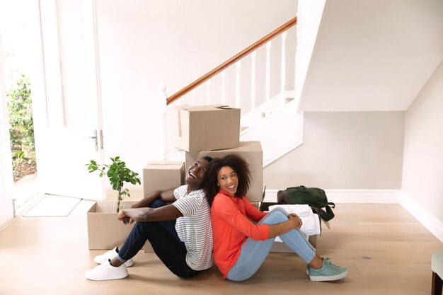 Foto vista lateral de um casal afro-americano em casa, se mudando, sentado no chão e recostado ao lado de caixas de papelão. família aproveitando o tempo em casa, conceito de estilo de vida
