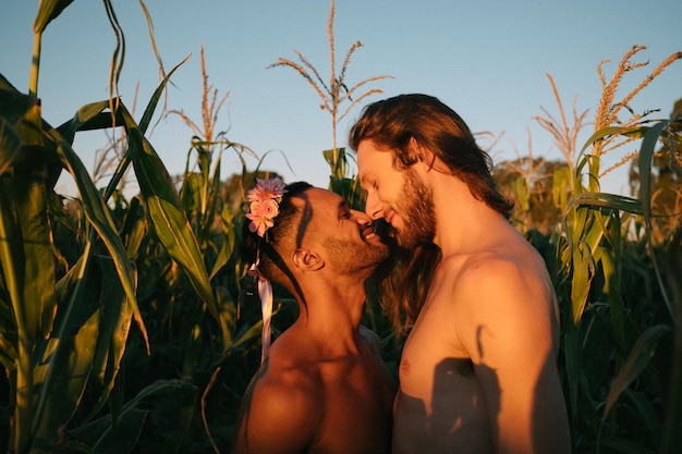 Vista lateral de um casal gay sem camisa fazendo romance enquanto está de pé em meio a plantas