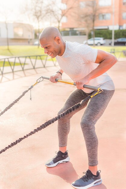 Vista lateral de um desportista atlético latino, exercitando-se com uma vara de ginástica elástica no parque. Homem adulto fazendo exercícios do lado de fora.