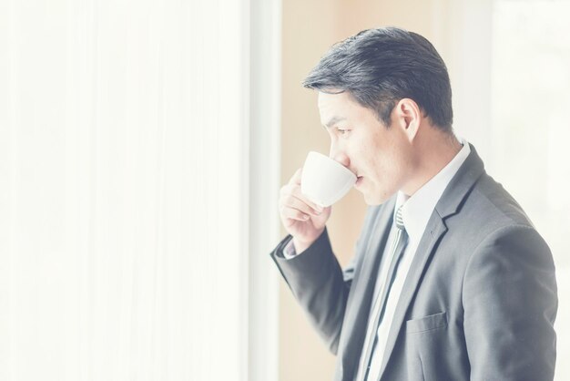 Vista lateral de um empresário bebendo café enquanto está de pé junto à janela em casa