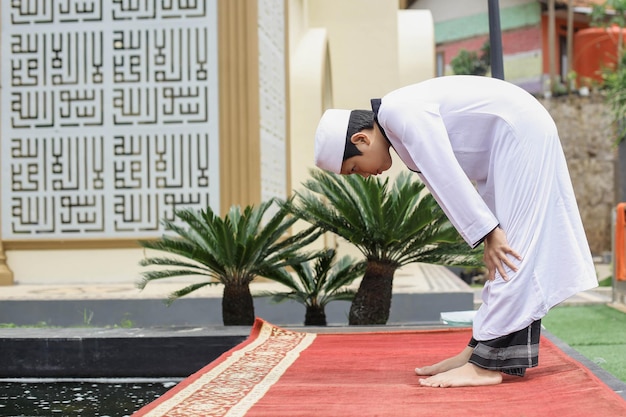 Vista lateral de um estudante de internato islâmico fazendo salat com rukuk posado ou curvado