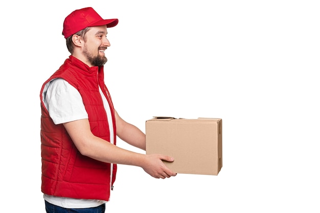 Vista lateral de um feliz adulto barbudo entregador de uniforme vermelho dando uma caixa de papelão durante a entrega de encomendas contra um fundo branco