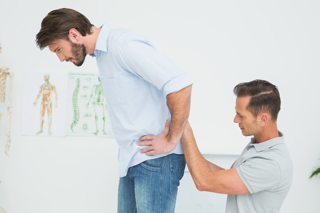 Vista lateral de um fisioterapeuta masculino examinando mans back
