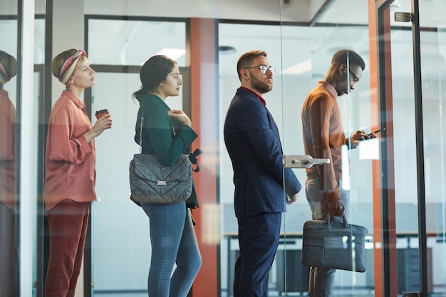 Vista lateral de um grupo multiétnico de executivos em pé na fila do escritório atrás de uma parede de vidro, copie o espaço