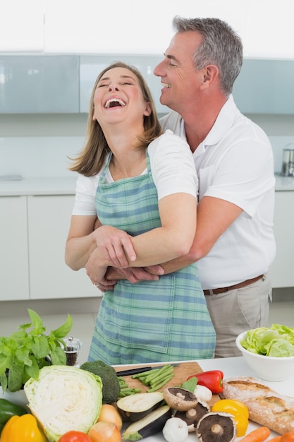 Vista lateral de um homem abraçando mulher na cozinha