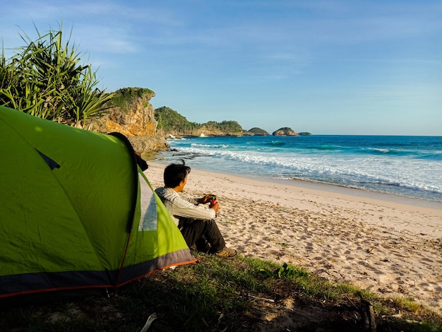 Foto vista lateral de um homem acampando na praia contra o céu