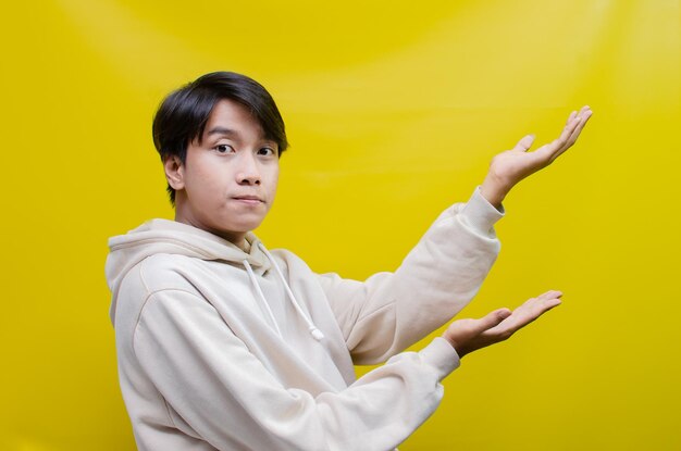 vista lateral de um homem asiático em um moletom bege apontando o dedo e abrindo os braços para promover anúncios