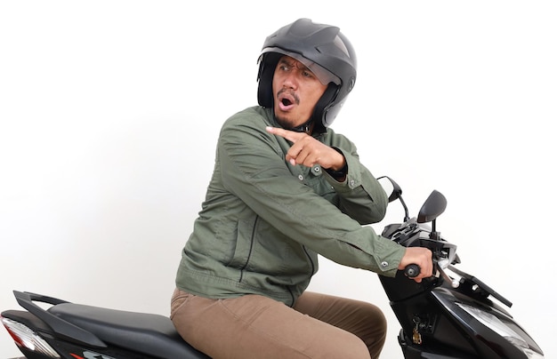 Foto vista lateral de um homem asiático zangado olhando para trás apontando e gritando enquanto dirige uma motocicleta isolado em fundo branco