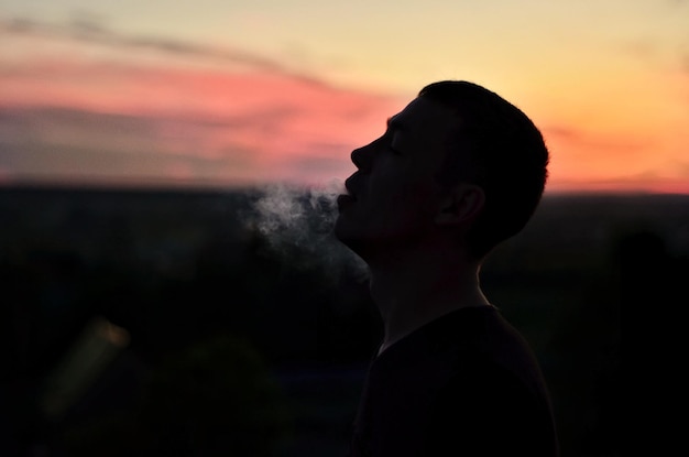 Foto vista lateral de um homem de silhueta fumando contra o céu durante o pôr do sol