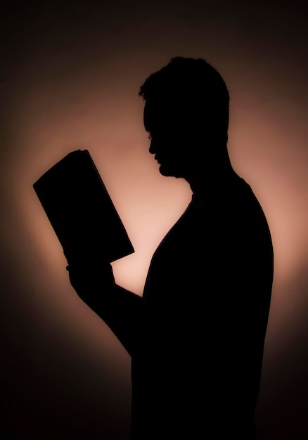 Vista lateral de um homem de silhueta segurando um livro contra a parede