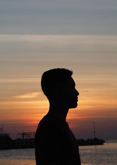 Foto vista lateral de um homem em silhueta contra o mar durante o pôr-do-sol