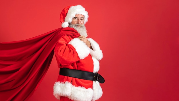 Vista lateral de um homem em traje de Papai Noel segurando um saco de presentes com espaço para cópias