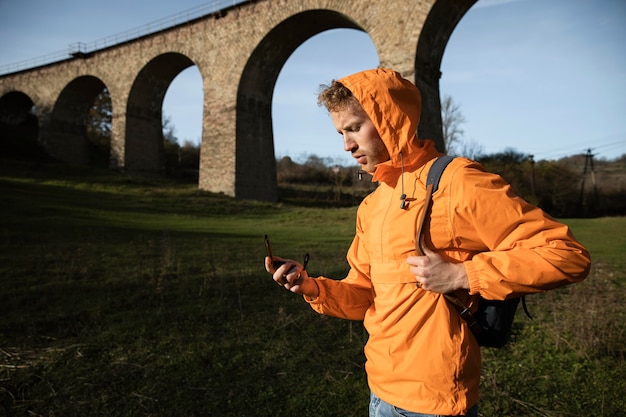 Foto vista lateral de um homem em uma viagem, posando em frente ao aqueduto, segurando uma bússola