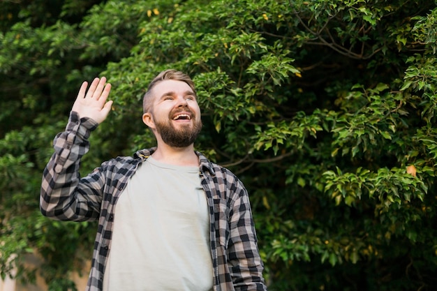 Foto vista lateral de um homem encantado ao ar livre e acenando com a mão para seu amigo, ele está feliz em conhecer seu