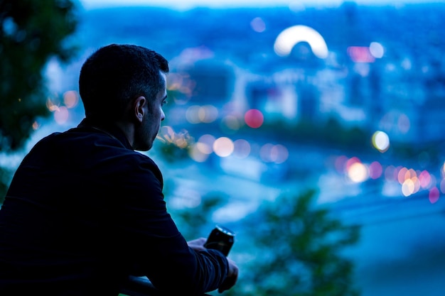 Foto vista lateral de um homem olhando para a cidade iluminada ao anoitecer