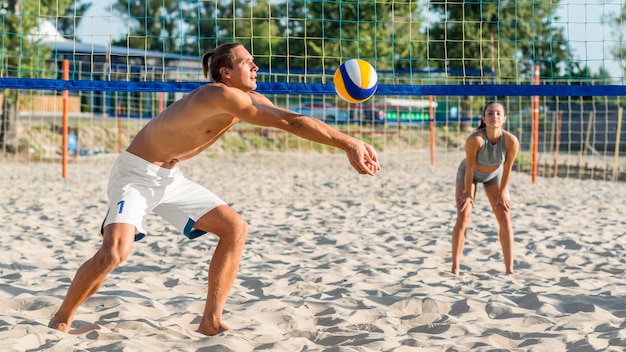 Vista lateral de um jogador de vôlei jogando na praia