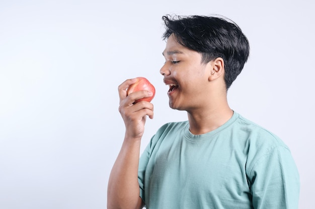 Vista lateral de um jovem asiático comendo maçã sobre um fundo branco Vida saudável e alimentação saudável conce