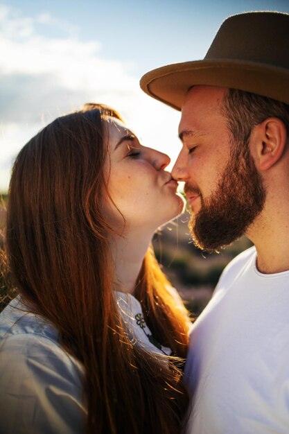Foto vista lateral de um jovem casal a beijar-se contra o céu