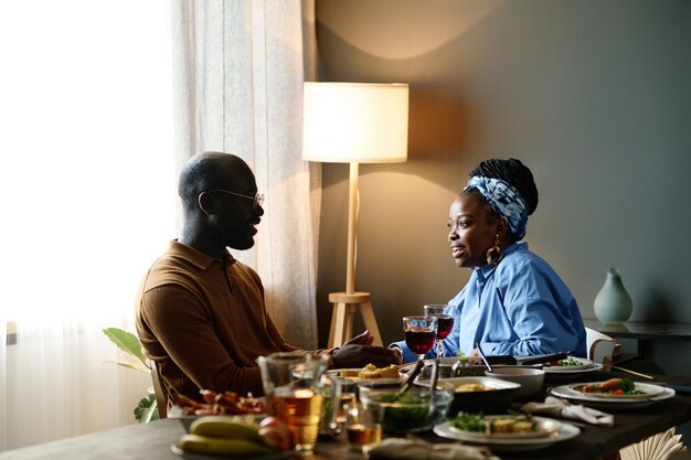 Vista lateral de um jovem casal afro-americano conversando em uma mesa festiva servida com comida caseira