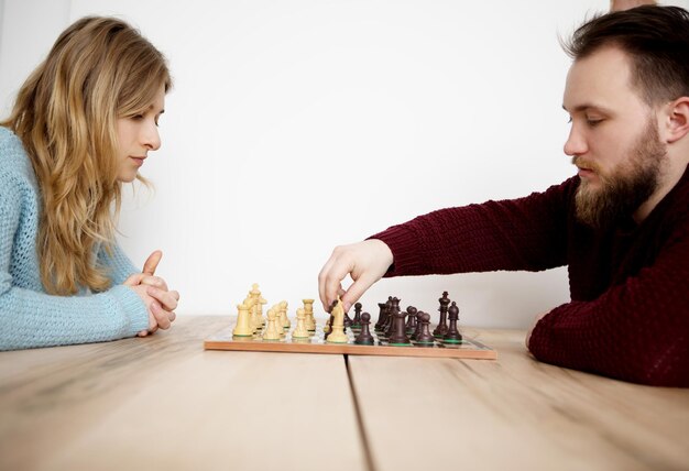 Foto vista lateral de um jovem e uma jovem jogando xadrez enquanto estão sentados na mesa em casa