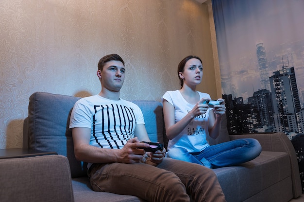 Vista lateral de um jovem e uma mulher tão apaixonados pelo processo de um jogo e sentados em um sofá em casa jogando videogame