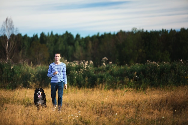 Vista lateral de um jovem homem caucasiano treinando Bernese Mountain Dog no campo de verão