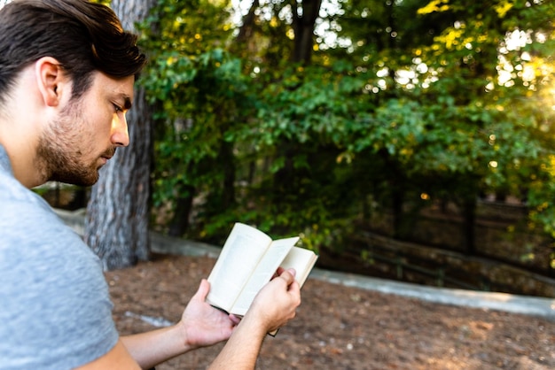 Foto vista lateral de um jovem lendo um livro contra as árvores