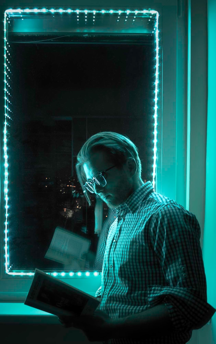 Foto vista lateral de um jovem lendo um livro sentado à janela à noite