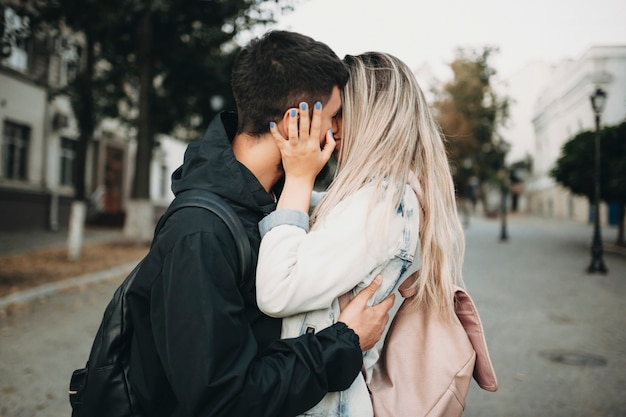 Vista lateral de um lindo casal apaixonado se beijando na rua enquanto se abraçava