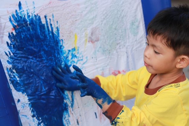 Foto vista lateral de um menino com mãos azuis pintando na parede