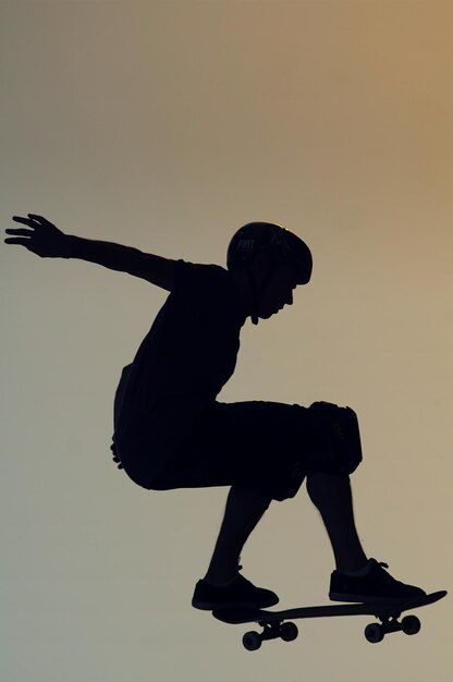Foto vista lateral de um menino em silhueta patinando contra um céu claro