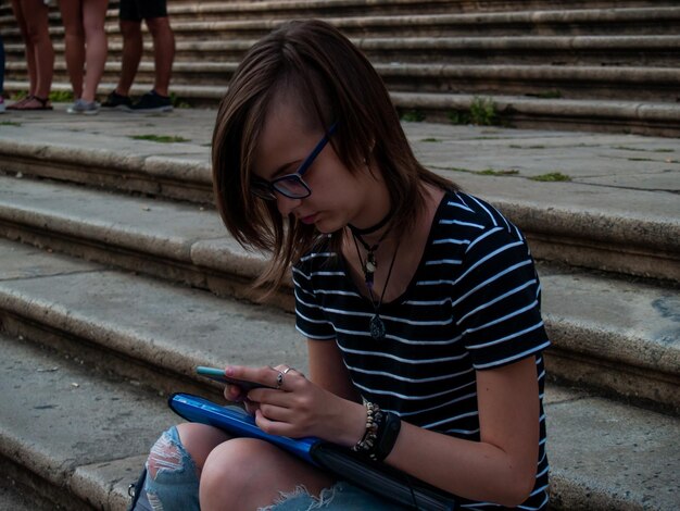 Foto vista lateral de uma adolescente usando um telefone celular enquanto está sentada nas escadas