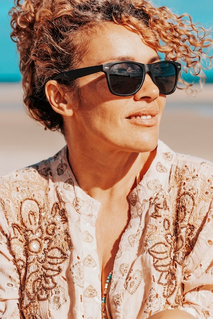 Foto vista lateral de uma bela mulher sentada na praia mulher loira com cabelos encaracolados soprando no vento relaxa olhando e sorrindo