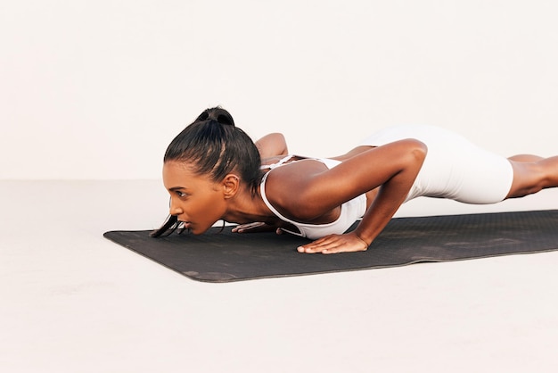 Vista lateral de uma desportista magro fazendo flexões em um tapete preto ao ar livre