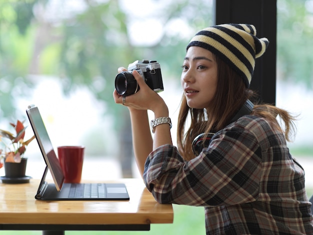 Vista lateral de uma fotógrafa tirando foto com a câmera enquanto está sentada em um café