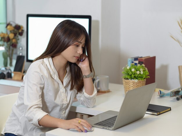 Vista lateral de uma funcionária de escritório trabalhando em casa com laptop e computador na sala de escritório