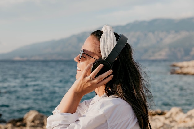 Vista lateral de uma jovem mulher de camisa branca ouvindo música em fones de ouvido estilo de vida de praia de verão