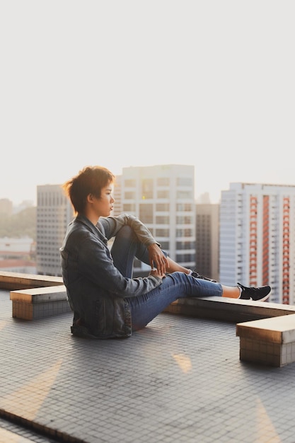 Foto vista lateral de uma jovem olhando para longe enquanto está sentada na cidade durante o pôr do sol