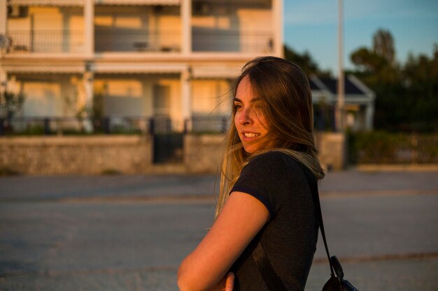 Foto vista lateral de uma jovem sorridente de pé contra um edifício na cidade