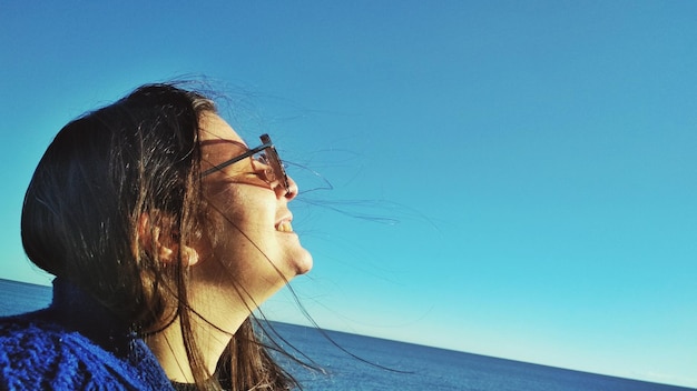 Foto vista lateral de uma jovem sorridente olhando para o mar contra o céu azul