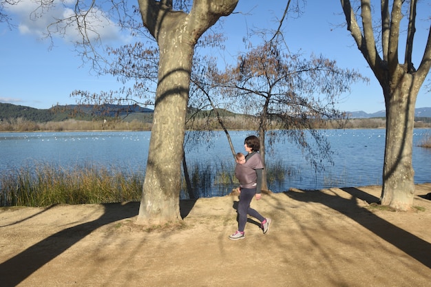 Vista lateral de uma mãe que faz exercícios carregando seu filho para fora