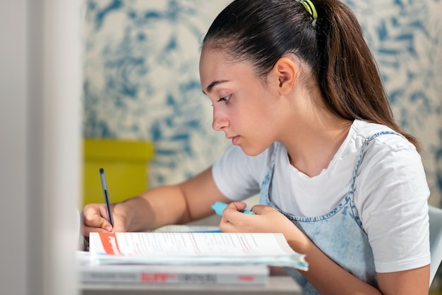 Vista lateral de uma menina adolescente inteligente focada escrevendo no caderno enquanto prepara a tarefa de casa na mesa em casa