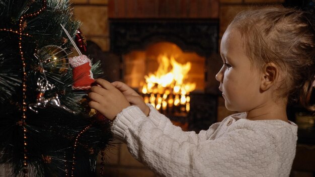 Vista lateral de uma menina de pé junto à árvore de Natal em casa