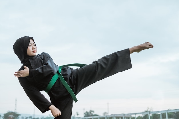 Vista lateral de uma mulher asiática com véu usando um uniforme de silat pencak com chutes retos