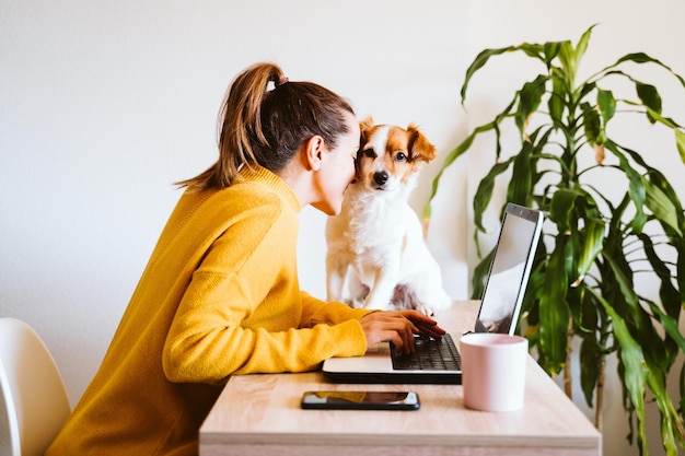 Vista lateral de uma mulher brincando com um cachorro enquanto usa um laptop