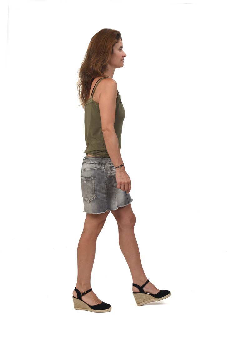 Foto vista lateral de uma mulher com saia jeans e spadrille andando sobre fundo branco